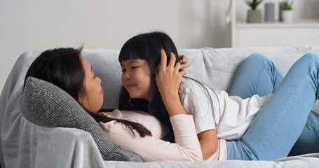 Asian mother hugs her beloved daughter, Korean woman lies with cute baby on sofa in living room enjoy rest woman kisses her daughter on nose touches her face with female hands, parental love concept