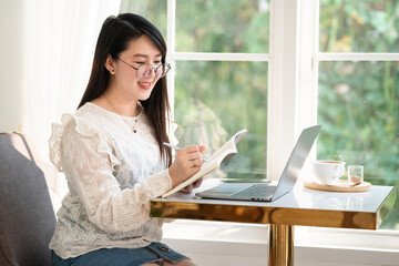 Happy of asian freelance people Businesswoman Taking written Notes to on notebook casual working with laptop computer with a coffee cup mug and smartphone at the cafe,Business Lifestyle
