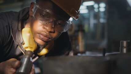 American industrial black young worker man with yellow helmet and ear protection surveillance for...