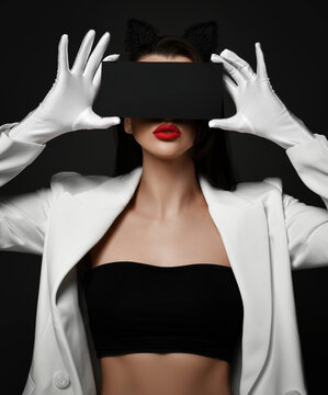 Beautiful brunette woman cosmetologist model in white jacket and gloves with red lips holding black mask over eyes over dark background. Wellness, cosmetology concept
