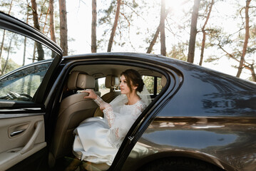 beautiful bride is sitting in the car. the bride prepares to leave the car for the ceremony. girl in a wedding dress.