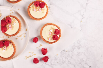 Small tartlet pastries with white cream, topped with raspberry fruits and almond sprinkles