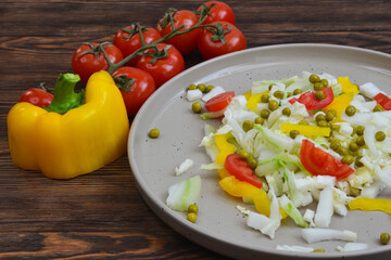 fresh summer vegetable salad with peking cabbage, cherry tomatoes, green peas and yellow bell pepper on a ceramic plate