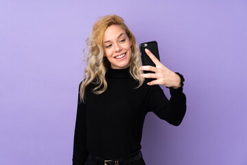Fototapeta premium Young blonde woman isolated on purple background making a selfie