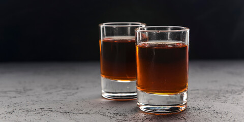 Two shot glasses with alcohol over black background. Alcoholic beverages, drinks.