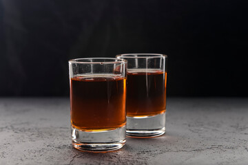Two shot glasses with alcohol over black background. Alcoholic beverages, drinks.