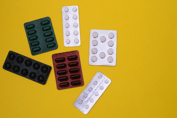 Blister packs of tablets and capsules in different colors. On a yellow background.