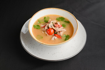 Mushroom soup of chicken broth, mushrooms, cherry tomato served in a white bowl over black background.