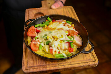 Close up healthy cooked main dish with veggies and melted cheese serbed by waiter in restaurant or diner.