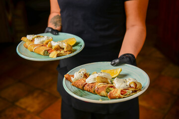 Savory crepe rolls with meat and vegetable filling served with sour cream by waiter in restaurant or diner.