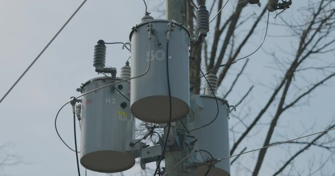 Close up of three Hydro transformers mounted on a wood hydro pole in the middle of the woods with spring trees in the background in Gatineau, Quebec. 