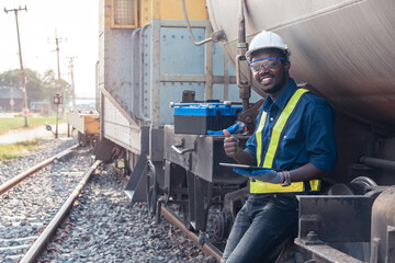 African machine engineer technician using tablet and wearing a helmet, groves and safety vest is using a wrench to repair the train