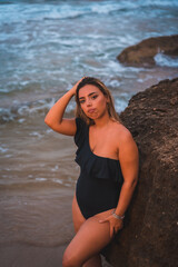 Lifestyle of a blonde Caucasian girl in a black swimsuit next to a rock in the sea