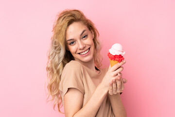 Young blonde woman holding a cornet ice cream isolated on pink background