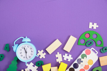 alarm clock, puzzles, dominoes, paints, glasses, educational toys on a purple background top view, back to school concept