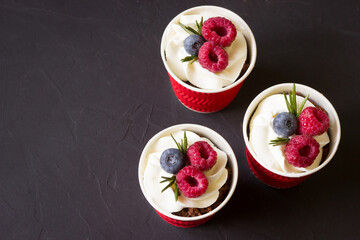 Dessert in a cups with cream cheese ,raspberries and blueberry, black background