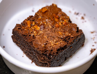 Close up of a Chocolate Almond Brownie in a white takeout box on a black granite background.