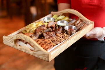 Mixed grilled meat with pepper sauce on a wooden board served by waiter in restaurant or diner.
