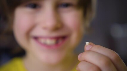 The boy's milk tooth fell out. A satisfied child holds a tooth in his hand. A hole in the gum is visible