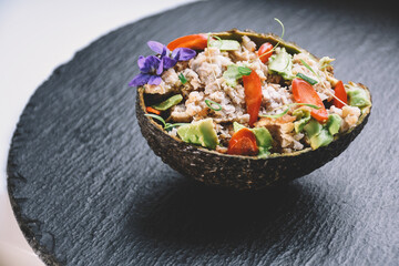 Avocado snacks, colorful, delicious, lie on a black slate plate. Stuffed with minced meat, avodako, bell pepper, dill microgreens, onions and decorated with a violet flower.