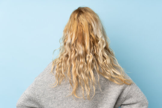 Young blonde woman wearing a sweater isolated on blue background in back position