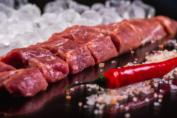 slicing for barbecue of fresh raw fresh meat on crushed ice with rosemary on a background of dark slate stone, top view. sloping horizon. Selective focus. Carnivores concept