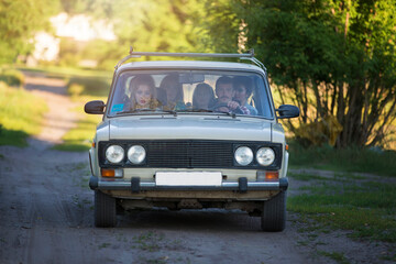 A cheerful company sits in the old car. Life in the 90s.