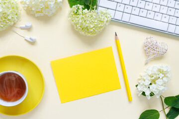 Top view of home office desk with laptop, cup of hot tea, and bouquet of hydrangeas  on yellow paper background.