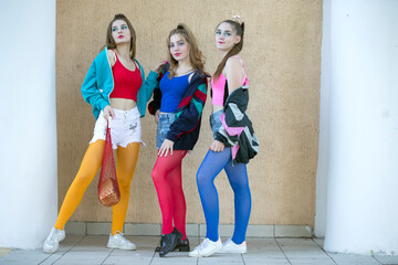 Three beautiful girls dressed in the style of the nineties are posing for the camera. - obrazy, fototapety, plakaty