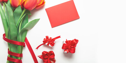 A bouquet of fresh tulips with envelope and a couple of packaged gifts with a red ribbon on a white background. Top view. Flat composition.