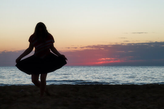 Silhouette of a teenage girl doing a curtsy on a beach at sunset at Golden Bay, Malta.