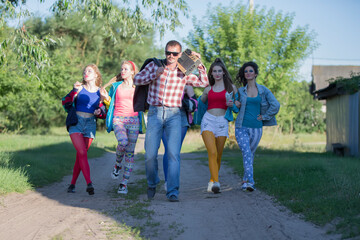 A funny guy with a cassette tape recorder and a group of beautiful girls are walking along the road.