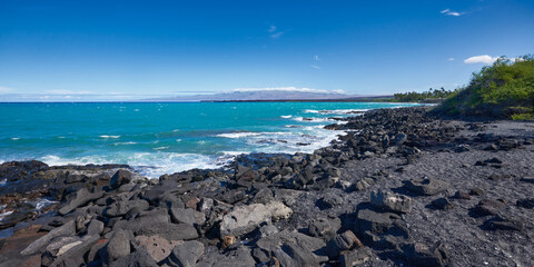 Panoramic view of the rocky coast with Mauna Kea volcano on the horizon in Hawaii on a sunny day.