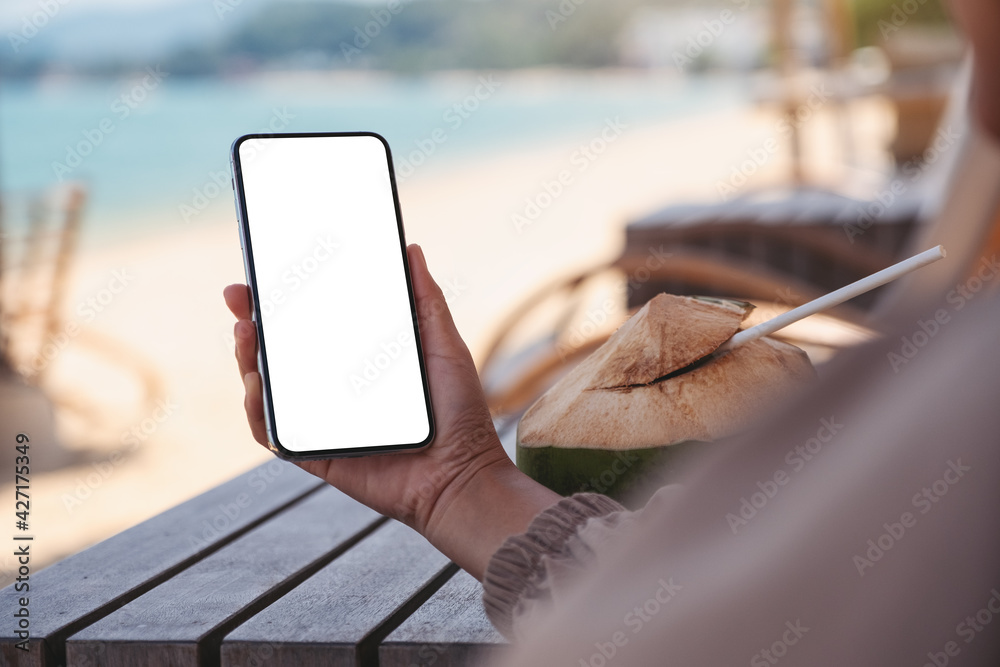 Wall mural Mockup image of a woman holding mobile phone with blank desktop screen on the beach