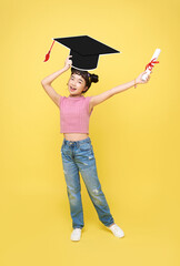 Happy Asian cute schoolgirl with graduation hat and diploma isolated on yellow background.