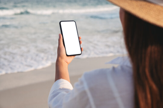 Mockup image of a woman holding mobile phone with blank desktop screen on the beach