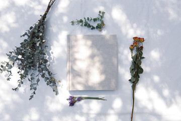 自然光と植物の影が差し込む、白のファブリックに置かれた本 - obrazy, fototapety, plakaty