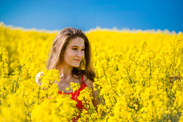 Beautiful, young woman in rapeseed field. Long hair, young smiling girl enjoying sun in blooming field.