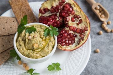Appetizer hummus of Turkish chickpeas on a white plate with half a pomegranate. Vegan food.