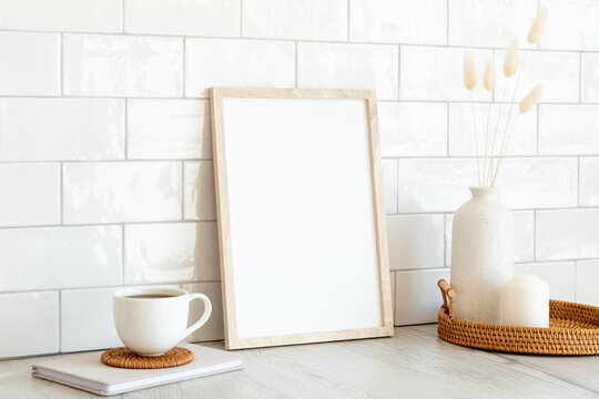 Vertical white photo frame mockup, cup of coffee, vase of dried flowers, candle on wooden table. Nordic, Scandinavian interior room design. Breakfast still life. © photoguns