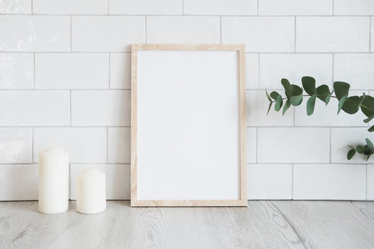 Empty photo frame mockup, candles, eucalyptus on table. Brick tiles wall on background. Scandinavian home decor, nordic style.