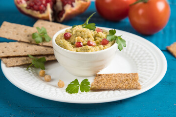 Close-up of a plate of Turkish chickpea hummus appetizer on a white plate with rye bread. Blue wooden background. Vegan food.