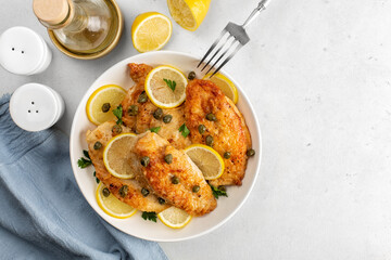 Chicken piccata on white table directly above. Chicken breast dredged in flour and cooked in sauce cantaining lemon juice, butter and capers.