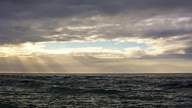 Cloudy ocean sunset over wavy ocean, time lapse