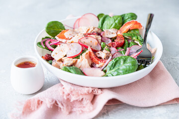 Fresh salad with salmon, spinach, radish and red oranges served with orange sauce, light concrete background.