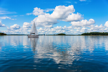 Sailing yacht in the lake with gloomy sky before the rain. Yacht sailing on the lake against a blue...