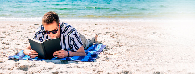 man lying relaxed on his towel on the beach reading a book