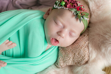 Baby girl in a wicker basket of vine decorated with  pink fur in a mint blanket and a flower wreath on her head. Spring photo. Flowers and children. Happy motherhood 