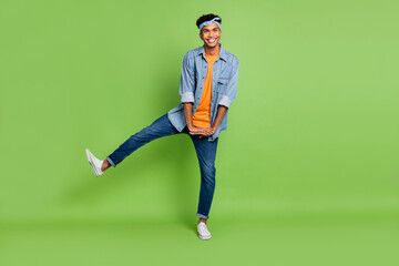 Full size photo of optimistic nice brunette guy dance wear blue shirt band jeans sneakers isolated on green color background