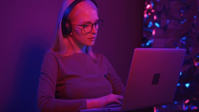Female working with headphones, a tablet and a laptop on a colorful neon light background. Close-up.